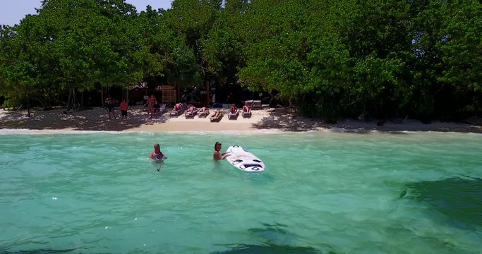 best friends girls swimming and trying to get on the paddleboard. aerial , tropical beach Bali