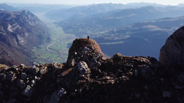 Dramatic aerial drone view of lone hiker reaching summit of mountain peak