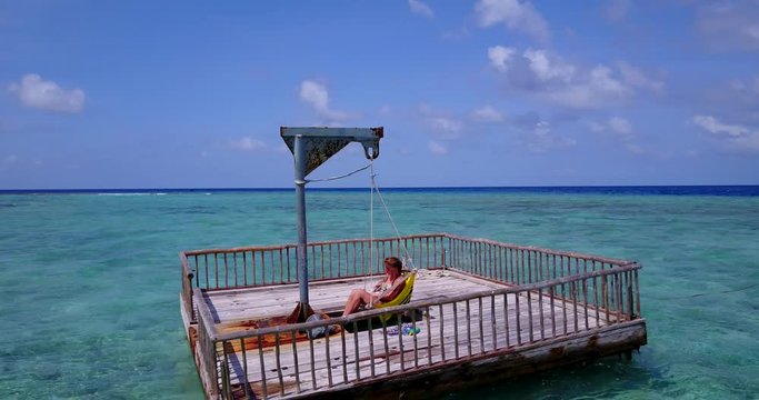 Young woman relaxing and reading a book in the swinging chair on a floating wooden raft. Open ocean