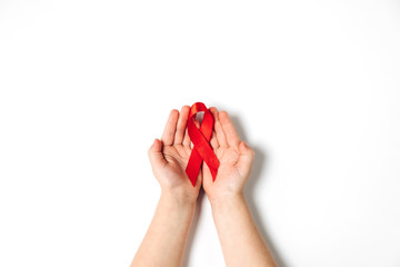 Top view on child's hands holding red ribbon on white background, HIV awareness concept, world AIDS day. Flat lay, copy space