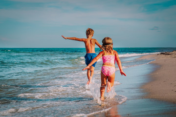 little girl and boy run and play with waves on beach