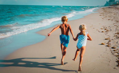 Fototapeta premium happy girl and boy run and play with waves on beach