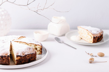 Homemade simple apple cake or pie sliced and sprinkled powdered sugar on grey concrete table decorated dry twig in vase. Autumn or winter treat. Fika. Hygge