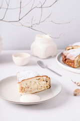 Homemade simple apple cake or pie sliced and sprinkled powdered sugar on grey concrete table decorated dry twig in vase. Autumn or winter treat. Fika. Hygge