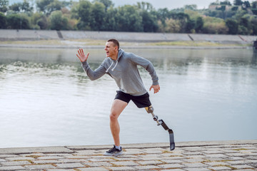 Fototapeta na wymiar Side view of healthy caucasian handicapped sportsman in sportswear and with artificial leg running on quay.