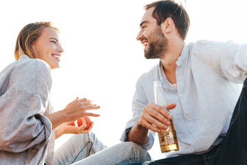 Lovely smiling young couple drinking beer, eating fruits