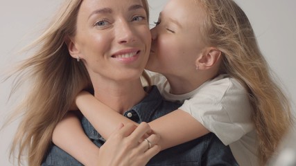 Mother with her teen daughter gives her a kiss and happy smiling mother watching to the camera