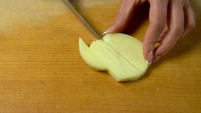 Potato slicing. female long fingers with a beautiful manicure with a knife cut potatoes into long slices on a wooden kitchen board close-up