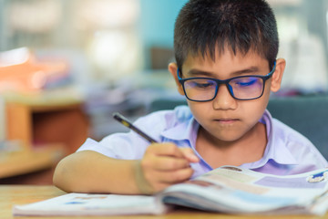 Asian elementary school boy in a white school uniform and wearing glasses, is doing homework in the...