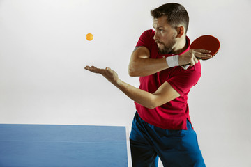 Young man plays table tennis on white studio background. Model in sportwear plays ping pong. Concept of leisure activity, sport, human emotions in gameplay, healthy lifestyle, motion, action, movement - obrazy, fototapety, plakaty