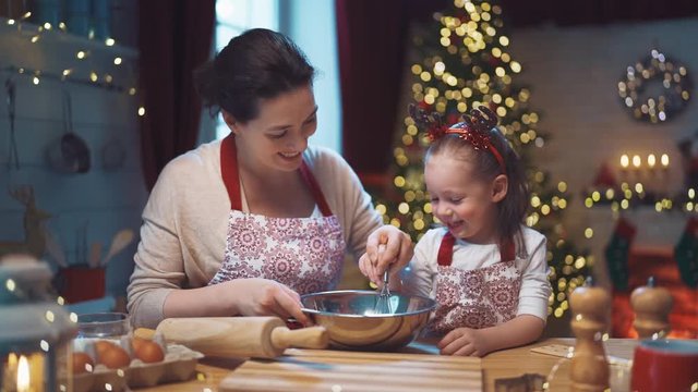 Merry Christmas and Happy Holidays. Family preparation holiday food. Mother and daughter cooking cookies.