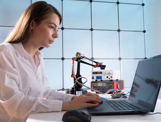 A young woman writes an algorithm for the robot arm. Science Research Laboratory for Robotic Arm...