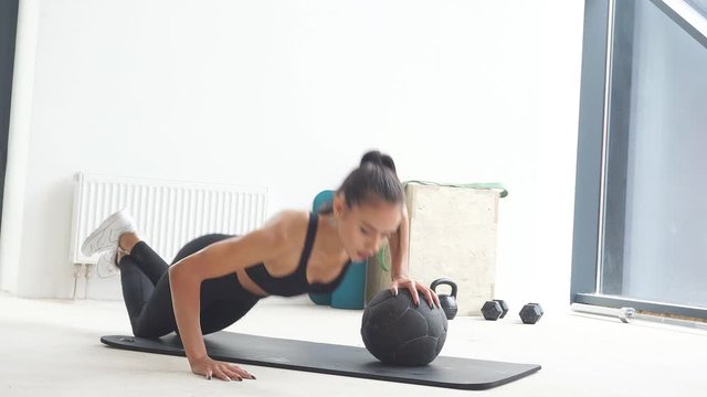 Attractive caucasian girl in sportswear do push up with ball. White gym background