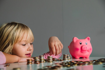 child saving money, cute girl put coins into piggy bank