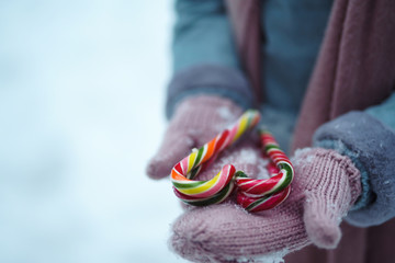 Christmas candy in the hands of a beautiful girl in the forest.The woman wears a blue coat, a light knitted hat, scarf and mittens.  Christmas striped candy canes. Sweets. New year surprise.