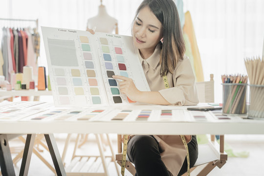 Asian designer woman discussing new paint colors comparing shades on a set of color in a shop.
