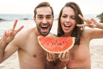 Photo of couple holding piece of watermelon and gesturing peace sign