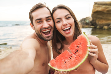 Photo of couple holding piece of watermelon and taking selfie photo