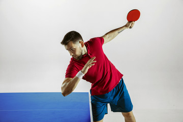 Young man plays table tennis on white studio background. Model in sportwear plays ping pong....