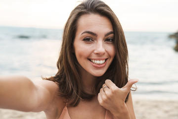 Image of smiling caucasian woman showing thumb up and taking selfie