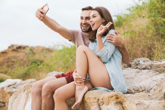 Photo of couple taking selfie photo on cellphone and gesturing peace