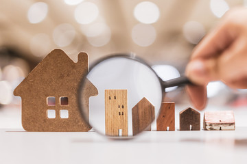 Hand holding magnifying glass and looking at house model, house selection, real estate concept.