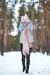 Cute young woman  is playing with snow  in the forest. The girl is dressed in a blue coat, in knitted hat, scarf and mittens. Winter lifestyle happiness emotions nature. Christmas, New year.