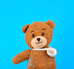 Obraz premium brown teddy bear with a bandaged paw sitting on a blue background