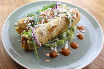 Delicious chicken burrito with salad, cheese, mayonnaise and ketchup on a white plate.
