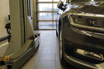 Modern car at a service and repair station, near with a lift. In the photo, the front of the car, the headlight, the bumper in focus and the lift in the background are blurred.