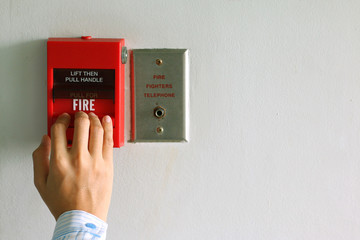 Hand of woman pulling fire alarm switch on the white wall as background for emergency case at the office