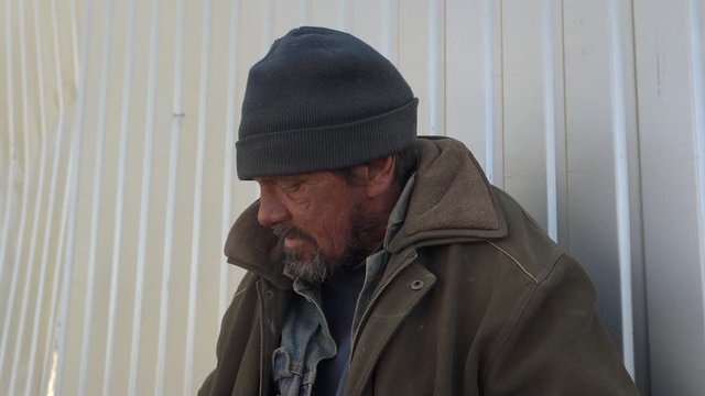 Homeless man during conversation outdoors. Beggar sitting on the street near the fence.