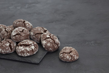 Chocolate crinkle cookies on dark slate plate, gray concrete background. Christmas, recipe concept. Close-up, copy space