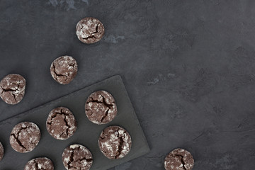 Chocolate crinkle cookies on dark slate plate, gray concrete background. Christmas, recipe concept. Top view, flat lay, copy space