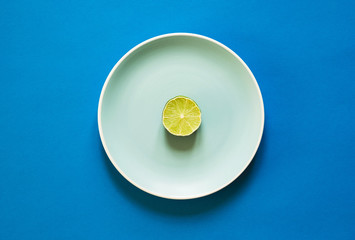 A slice of fresh lime on color plate on blue background. Flat lay.