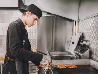 Burger making Food concept Young cook in black uniform is roasting beef for hamburgers on cafes...