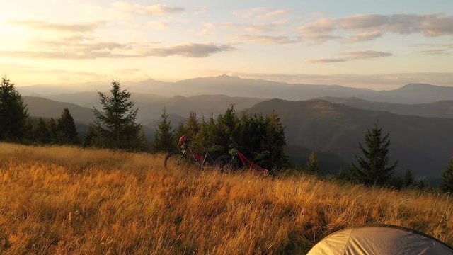 4k drone clip with two mountain bikes and a tent on a mountain meadow at sunrise in autumn season. Adventure cycling concept.