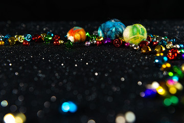 Colourful felted Christmas baubles and jingle bells. Black glitter and bokeh background. Shallow depth of field. Copy space.