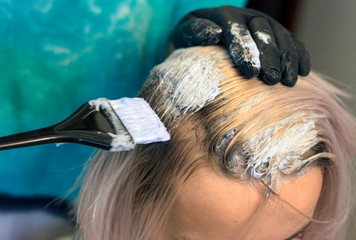 Naklejka premium Hair coloring Hairdresser in black gloves with a brush paints the roots of hair to a girl with a light color
