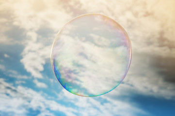 Flying huge soap bubble in cloudy sky.