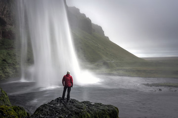 Obraz premium A man with red jacket by the famous icelandic waterfall, Seljalandsfoss early in the morning.