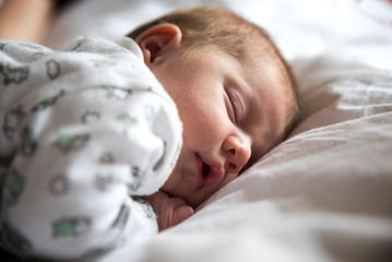 adorable bebé durmiendo en la cama entre sábanas blancas