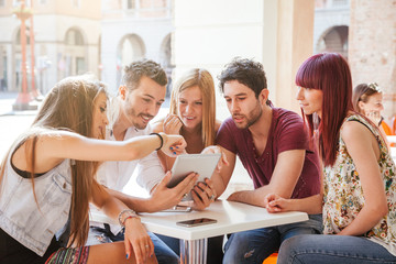 Millennials have fun together - Five friends looking tablet sitting at the table in a square in the city