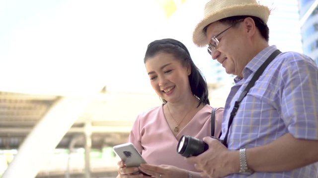 happy asian Senior couple tourists traveling using smartphone taking selfie photo together in urban city outdoors. old man Travellers lifestyle  . elderly woman vacation . ageing society concept.