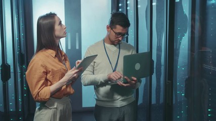 Couple of server IT engineers collaborating in data center inspecting supercomputer server rack updating hardware. Information technology. Teamwork. - Powered by Adobe