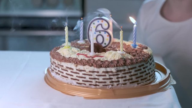 Closeup on birthday cake with lighted candle in shape of number six on it. boy in white t-shirt sitting at table at kitchen blowing candles on pie, making wish. Celebrating at home