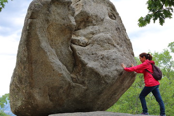 Mujer intentando el reto de empujar una roca gigante con esfuerzo en una aventura de senderismo