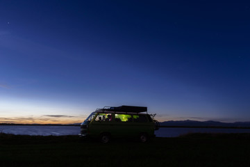 Sunset blue sky and camper van silhouette on the beach near the sea. Free parking and traveling through beautiful landscape - Image
