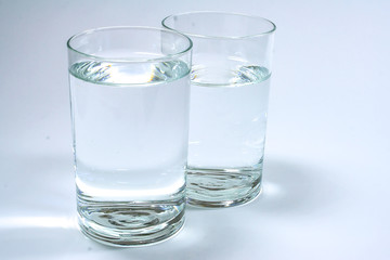 Two transparent glasses filled with clean water on a white background.