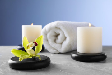Spa stones with exotic flower and burning candles on grey table, space for text